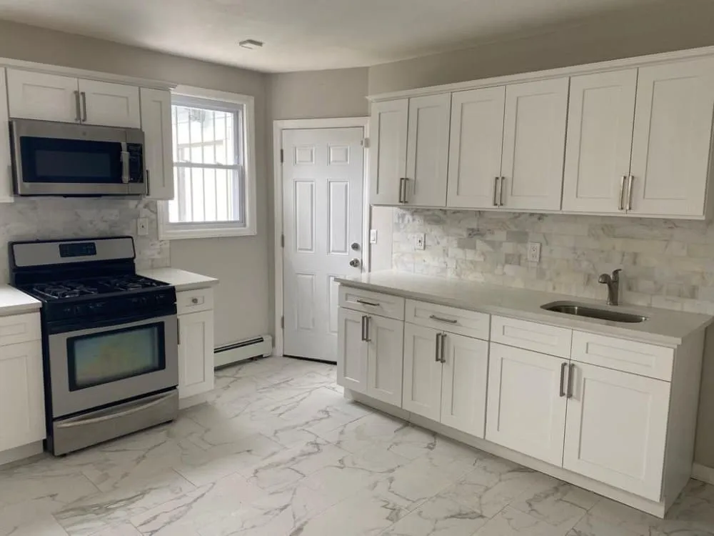 Renovated kitchen with white shaker cabinets and marble-look tile